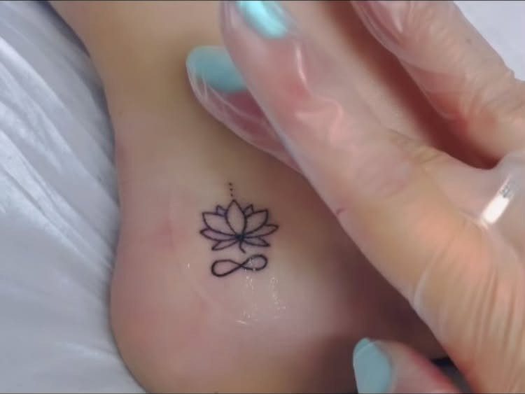Small lotus flower and infinity symbol tattoo on a person's ankle