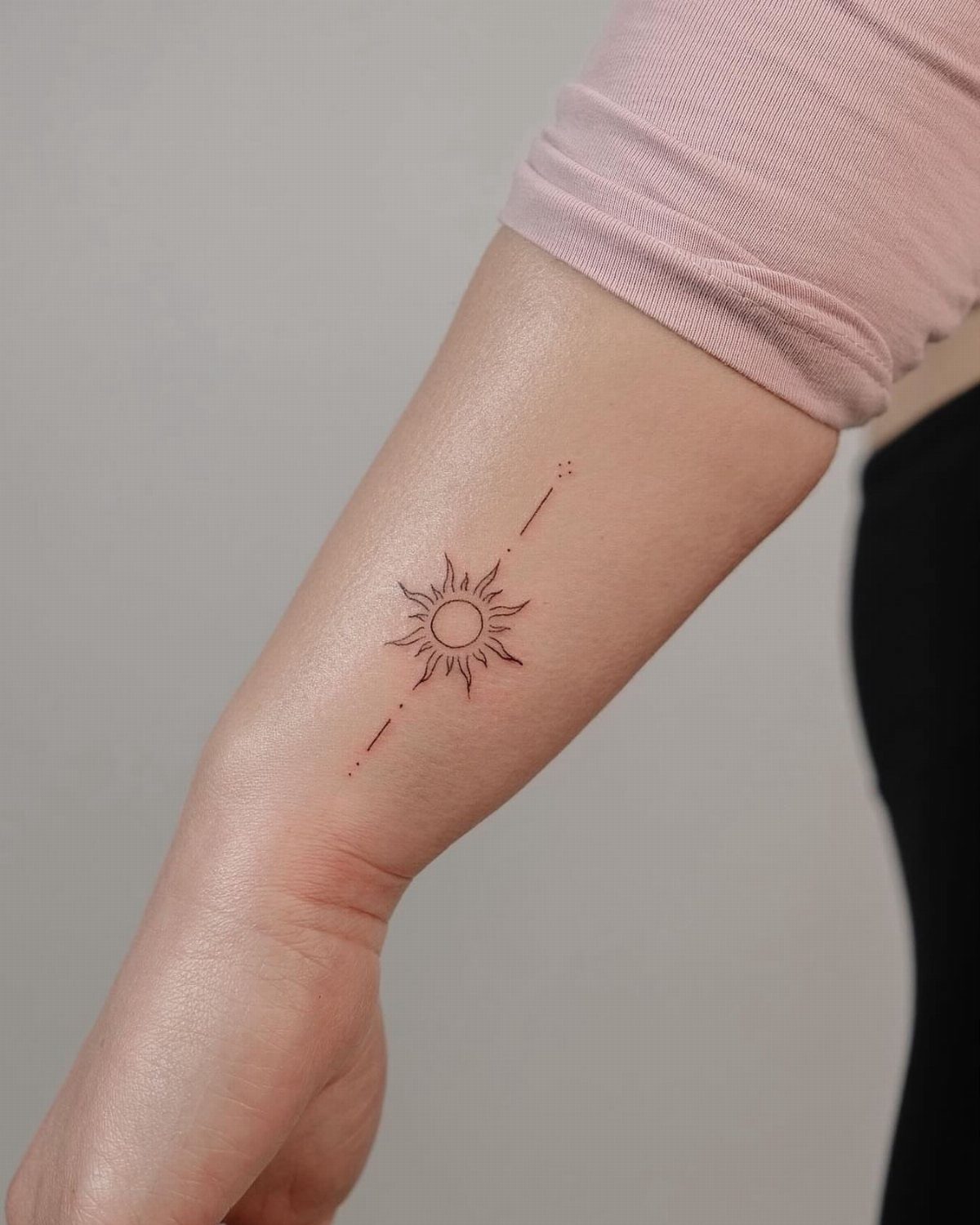Small sun tattoo with fine lines and dots on a person's inner forearm.