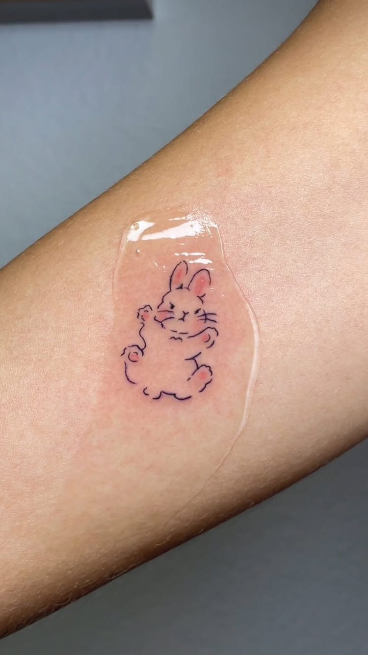 Small pink bunny rabbit tattoo with blue outlines on a person's arm.