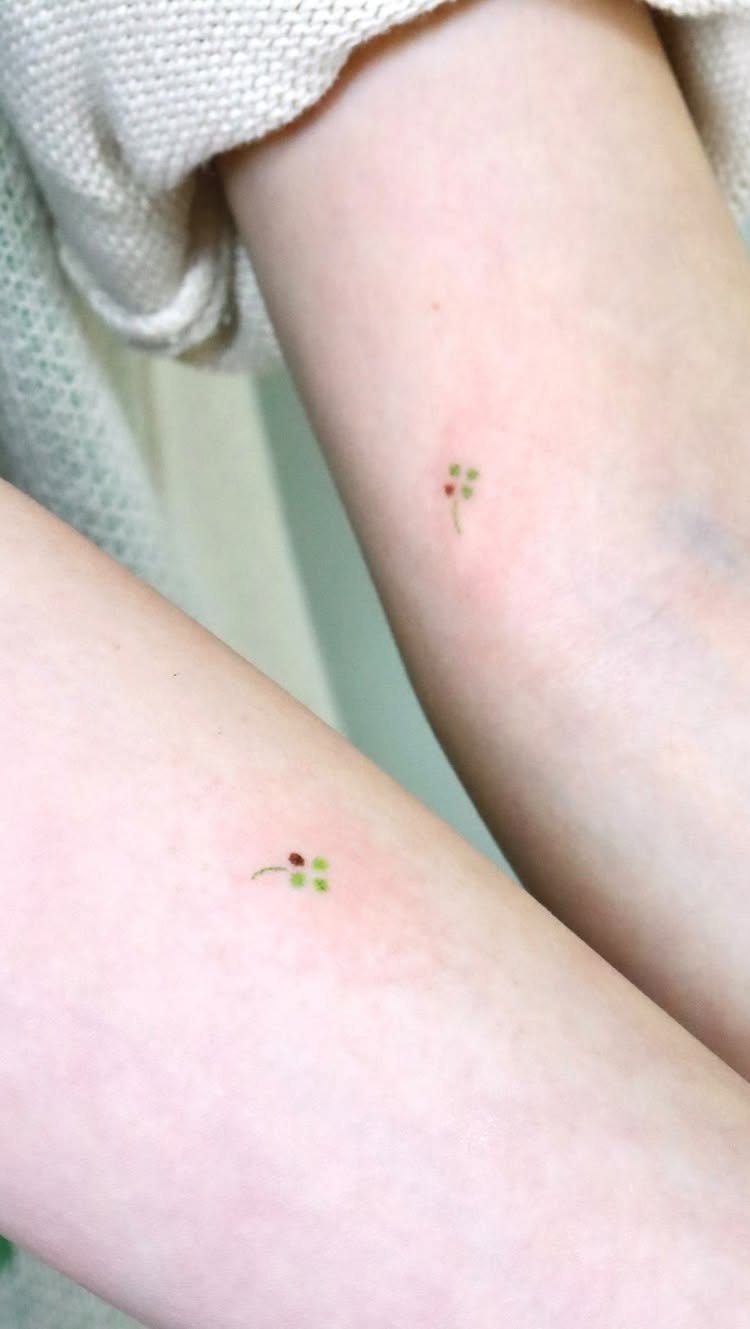 Two small four-leaf clover tattoos on the inner arms of a person.