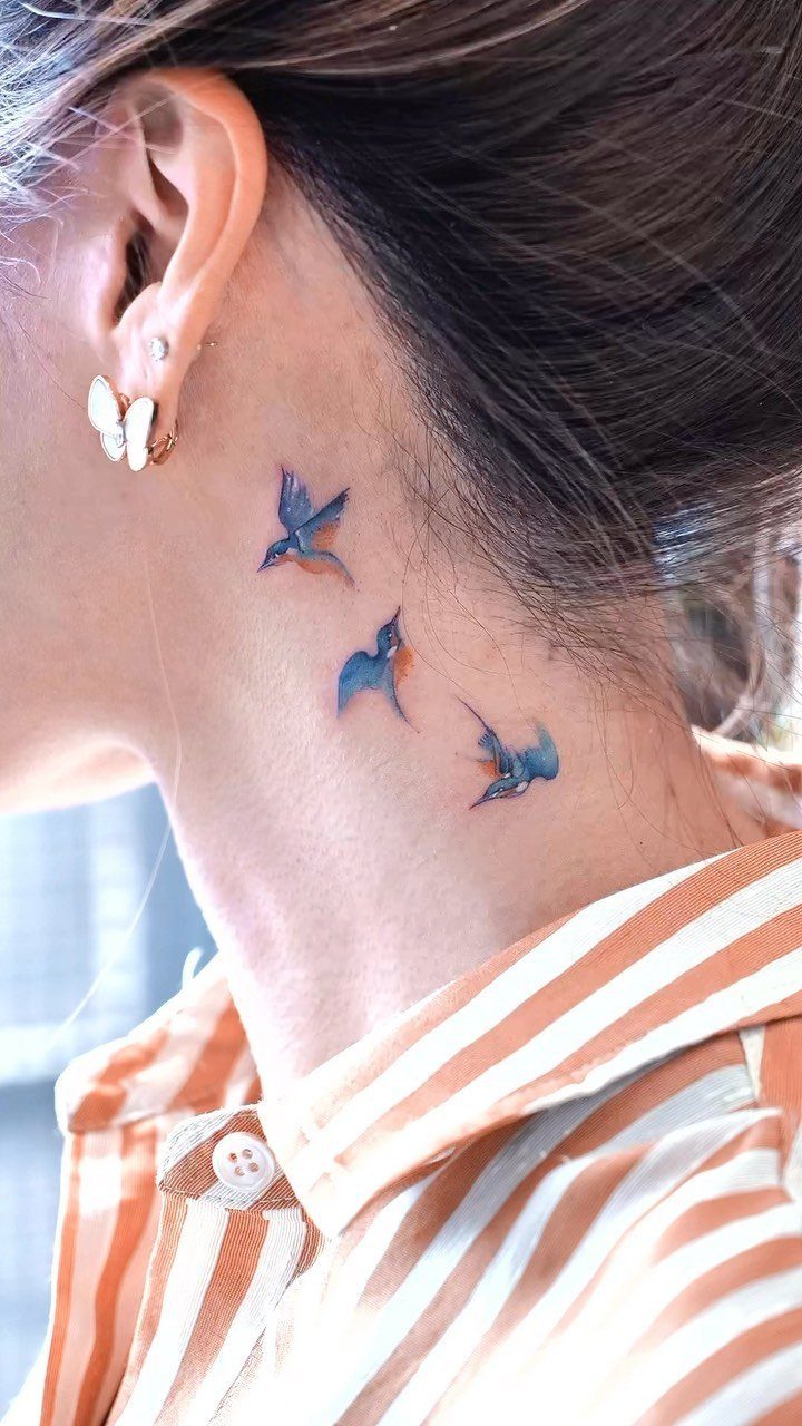 Three small blue bird tattoos on the side of a woman's neck.