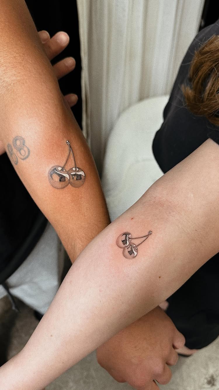 Two small cherry tattoos on the forearms of two different people.