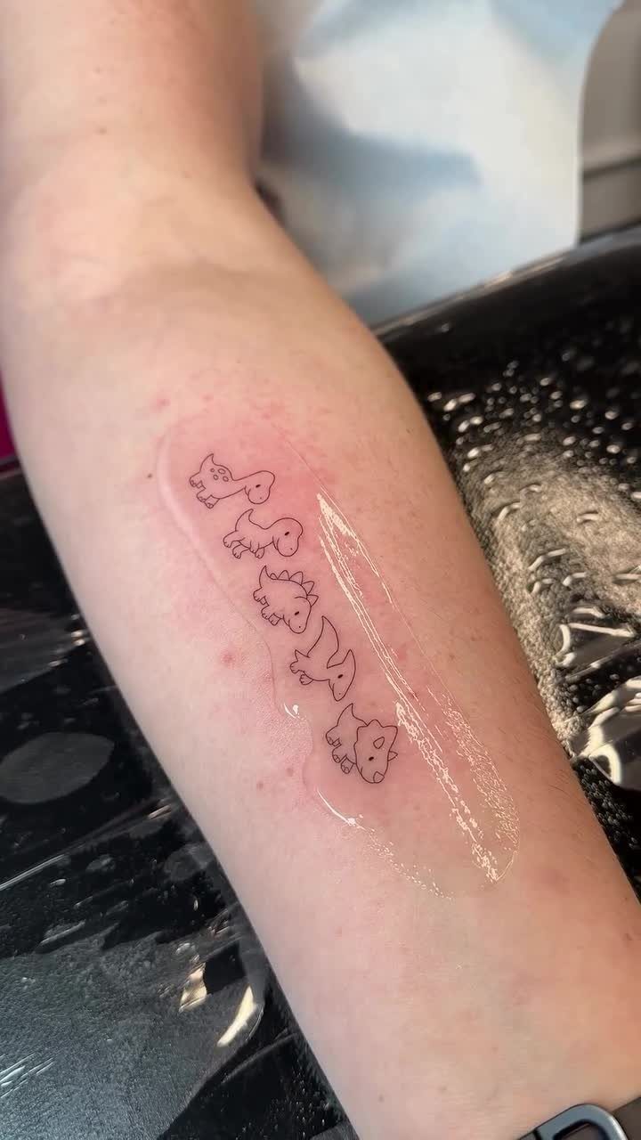Five small cute dinosaur outline tattoos in a row on a forearm.