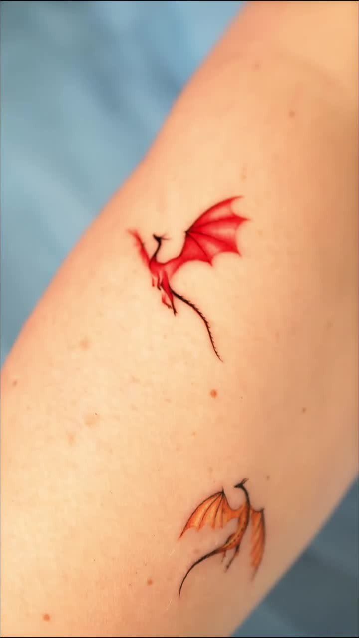 Two small colorful dragon tattoos, one red and one orange, on skin.