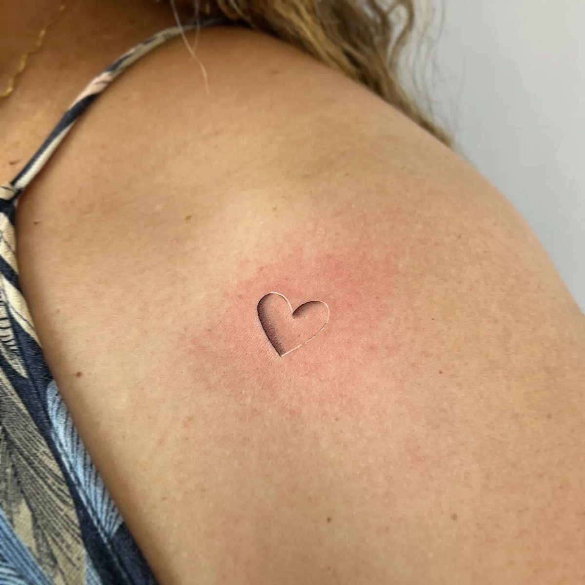 Small heart tattoo on a person's shoulder with slight redness around the ink.