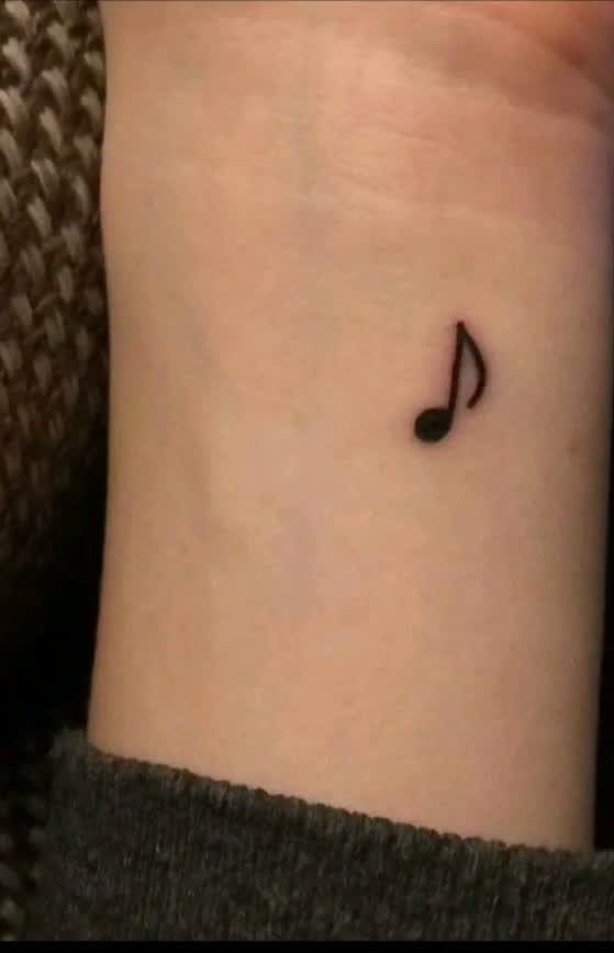 Small black musical note tattoo on the inside of a person's wrist.