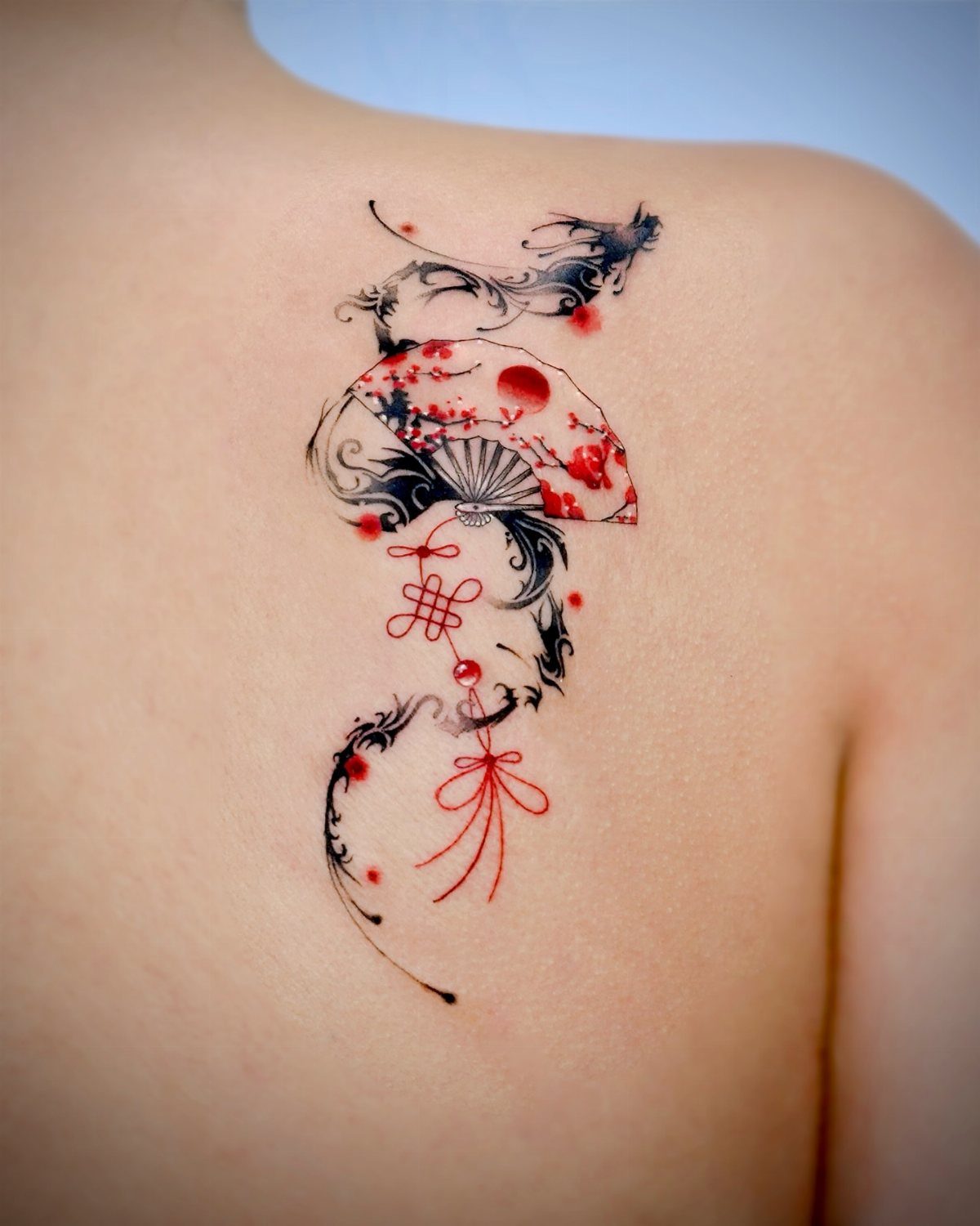 Tattoo of a red and black Japanese fan with floral details on a shoulder