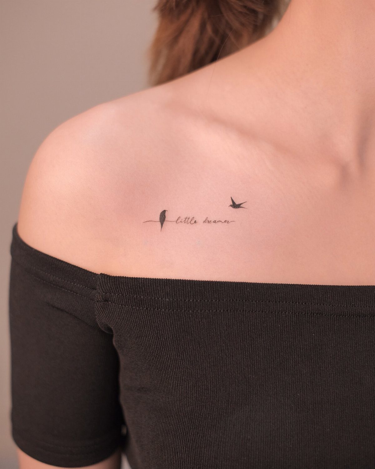 Small cursive tattoo saying little dreamer with birds on a person's shoulder