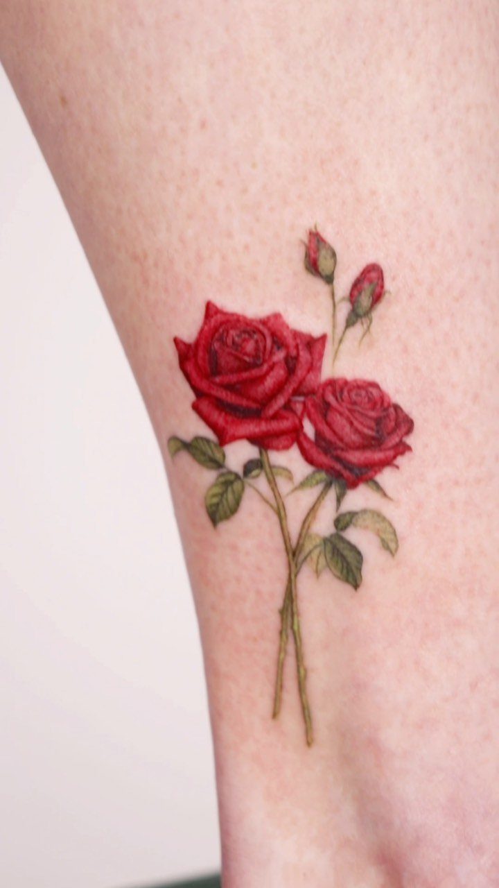 Two red rose tattoos with green leaves and buds on fair skin.