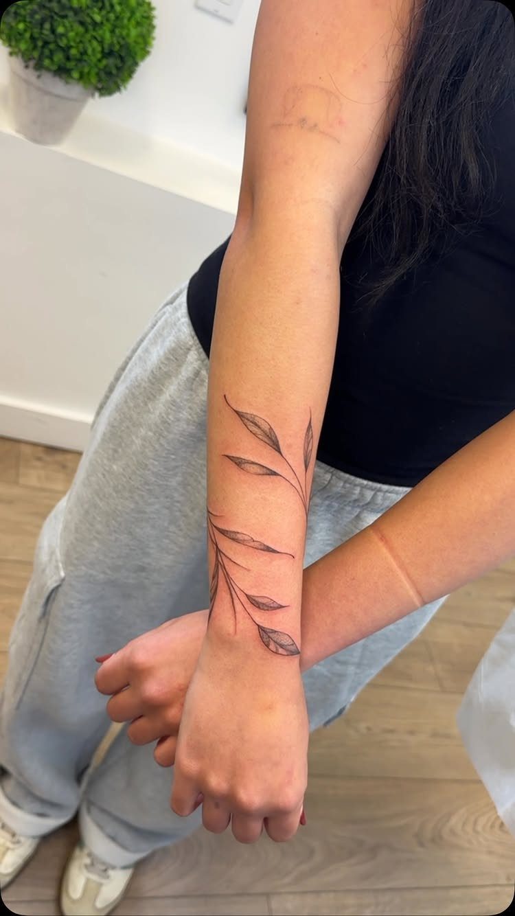Delicate black ink twig tattoo with leaves on a person's inner forearm