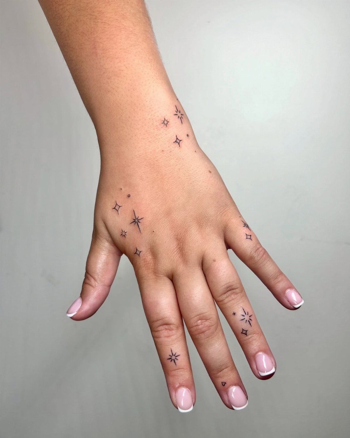 Hand and wrist with multiple small black star tattoos and French manicure nails.