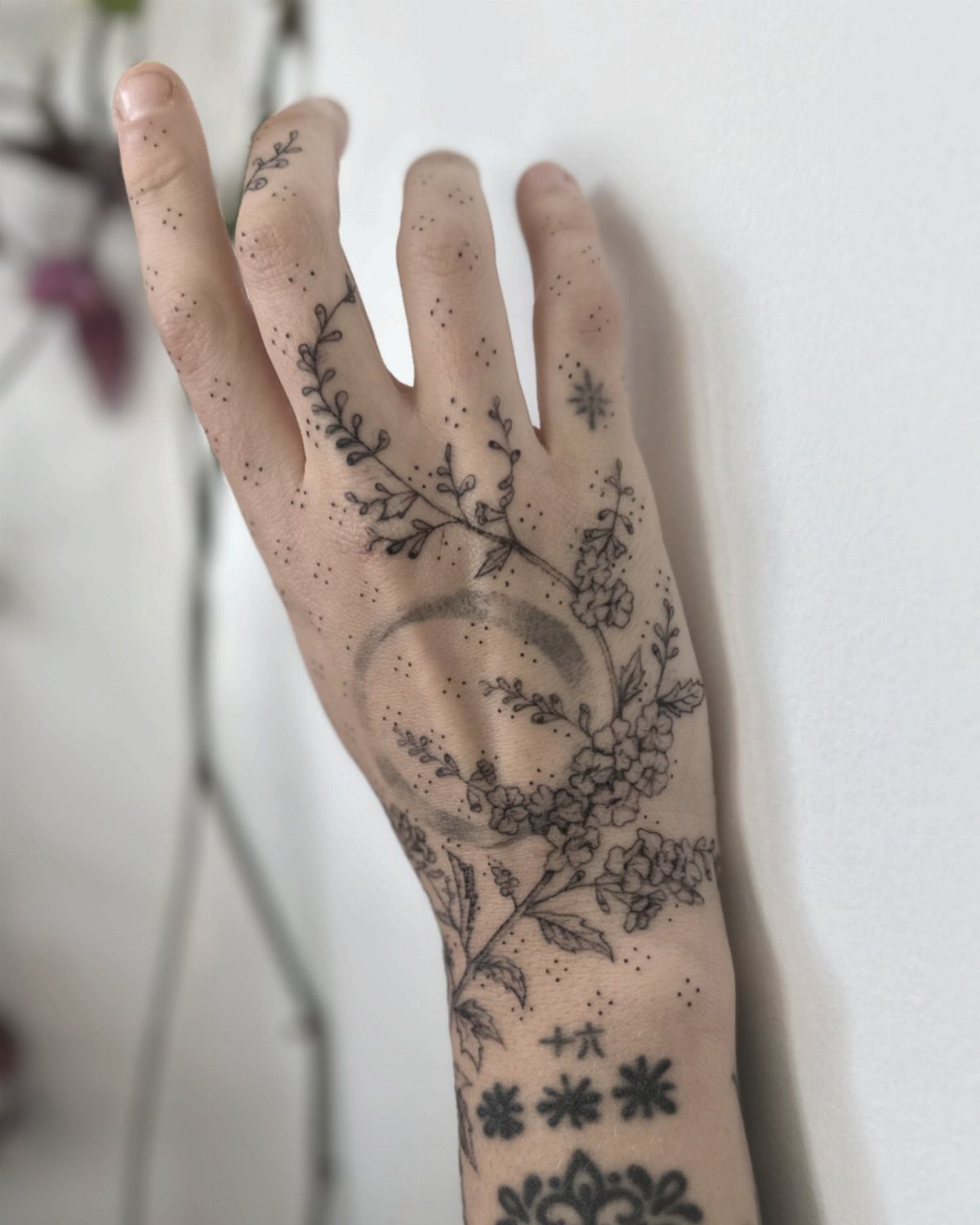 Hand and wrist with botanical line work tattoos of flowers and vines.