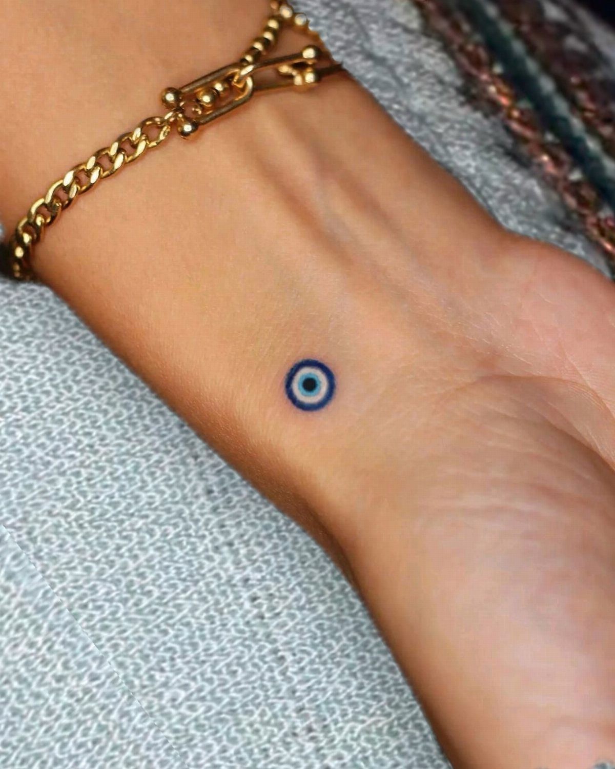 Small blue evil eye tattoo on the back of a person's hand.