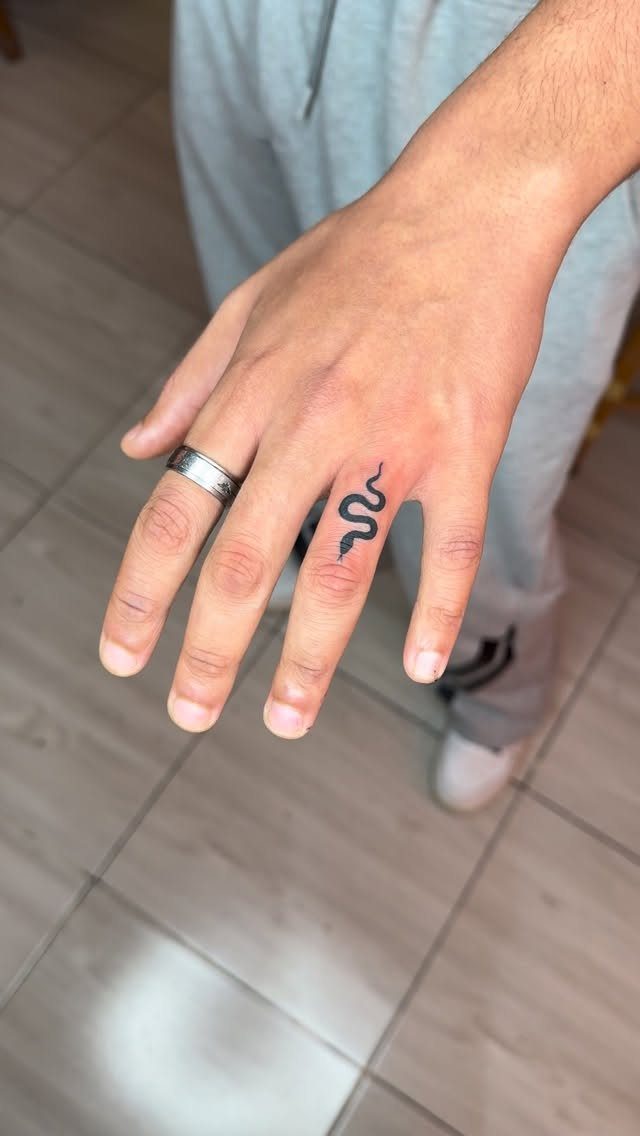 Hand with a small black snake tattoo on the ring finger and silver ring.
