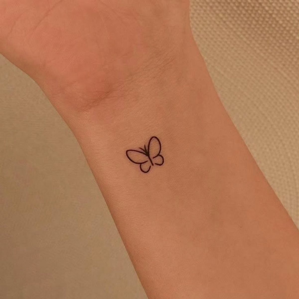 Small black butterfly tattoo on the side of a person's wrist and hand.