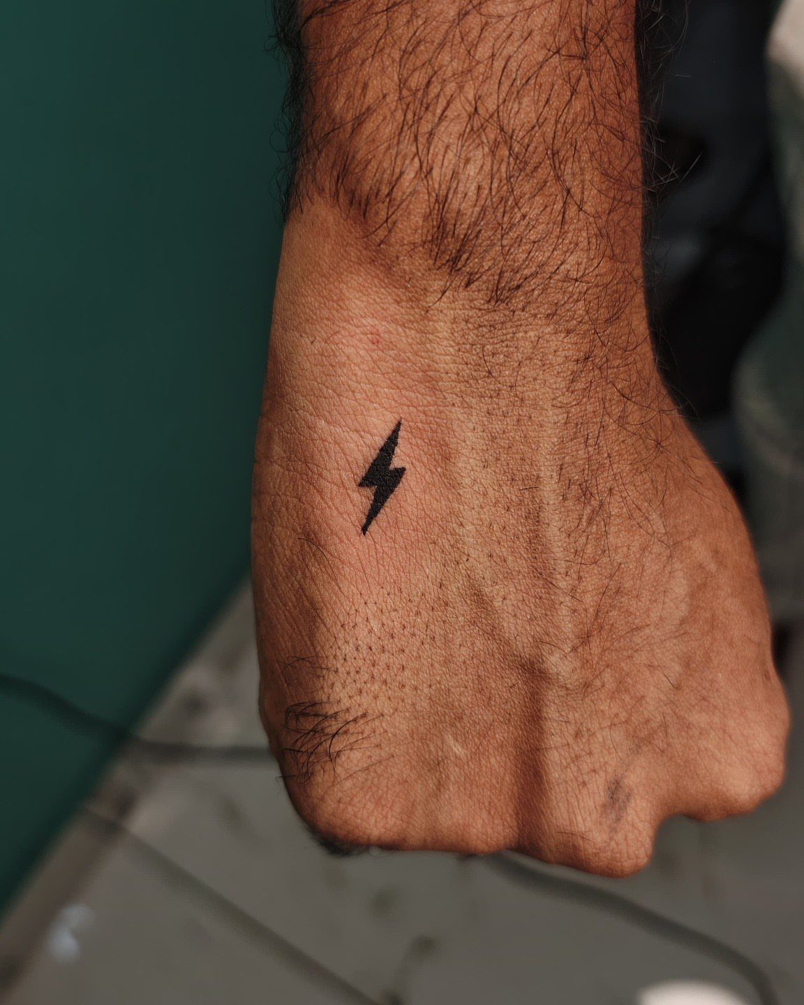 Small black lightning bolt tattoo on the back of a hairy hand.