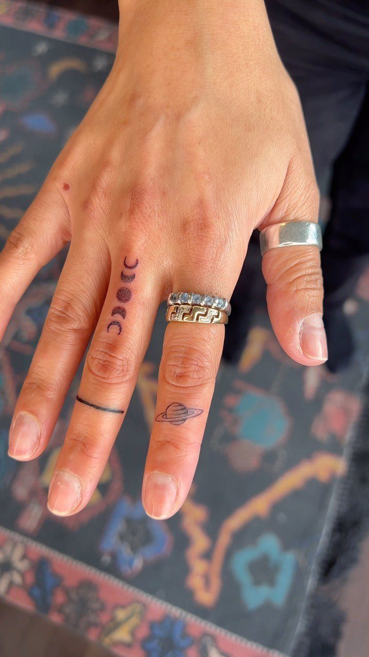 Hand with small black tattoos of a planet, a band, and vertical symbols.