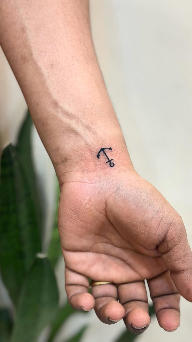 Small black anchor tattoo on the inner wrist of a person's hand.