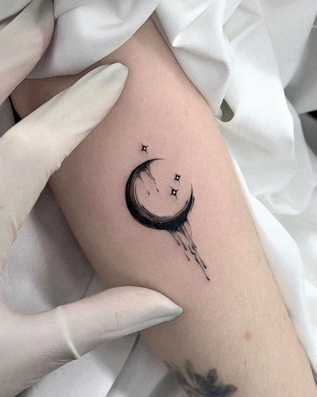Crescent moon tattoo with dripping ink and small stars on a person's arm