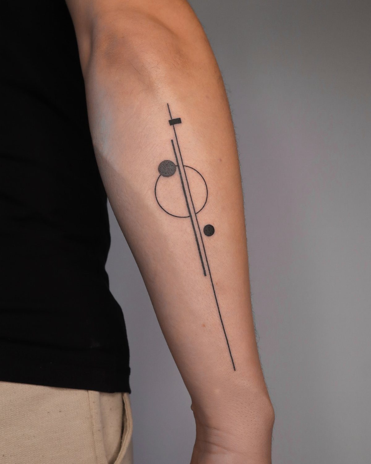 Geometric tattoo on an arm featuring a vertical line, circle, and minimalist shapes.