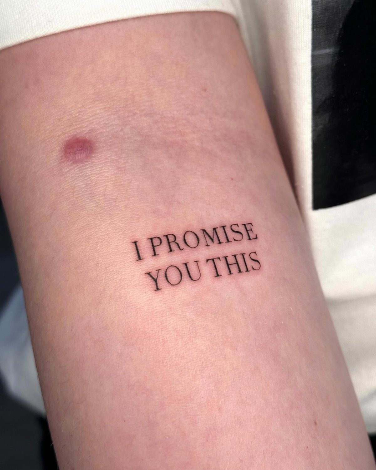 Small black ink tattoo on a forearm reading I PROMISE YOU THIS