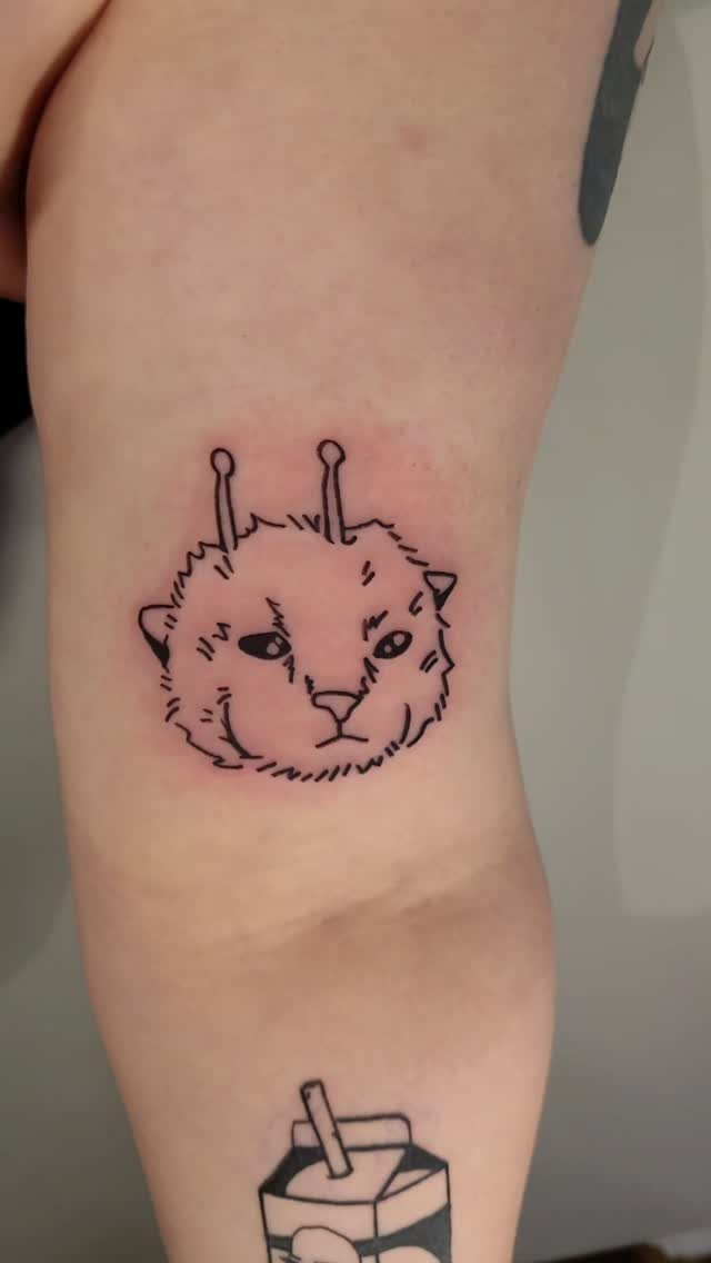Small black ink tattoo of a fluffy animal face on a person's arm.