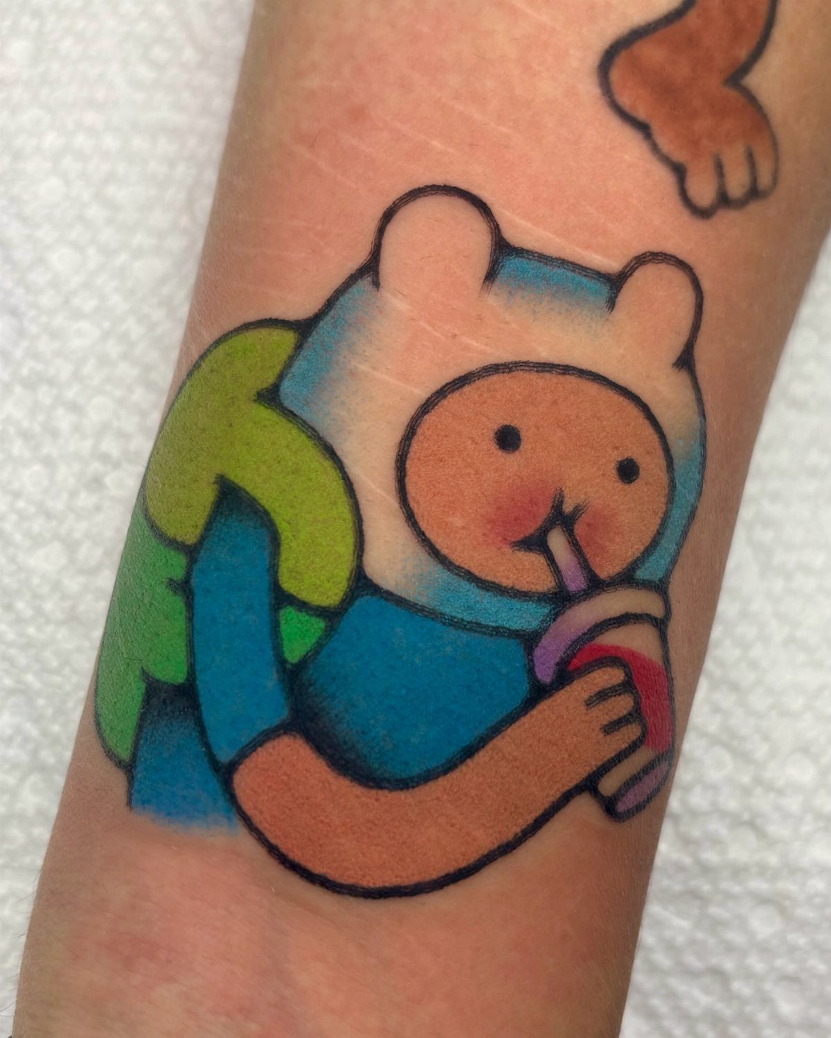 Cartoon character tattoo with a white hood and blue body drinking from a cup.