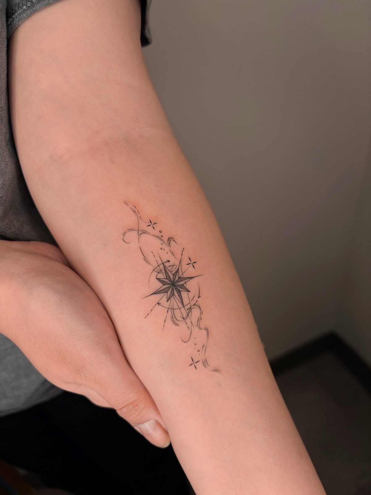 Small star tattoo with swirling lines and sparkles on a person's forearm