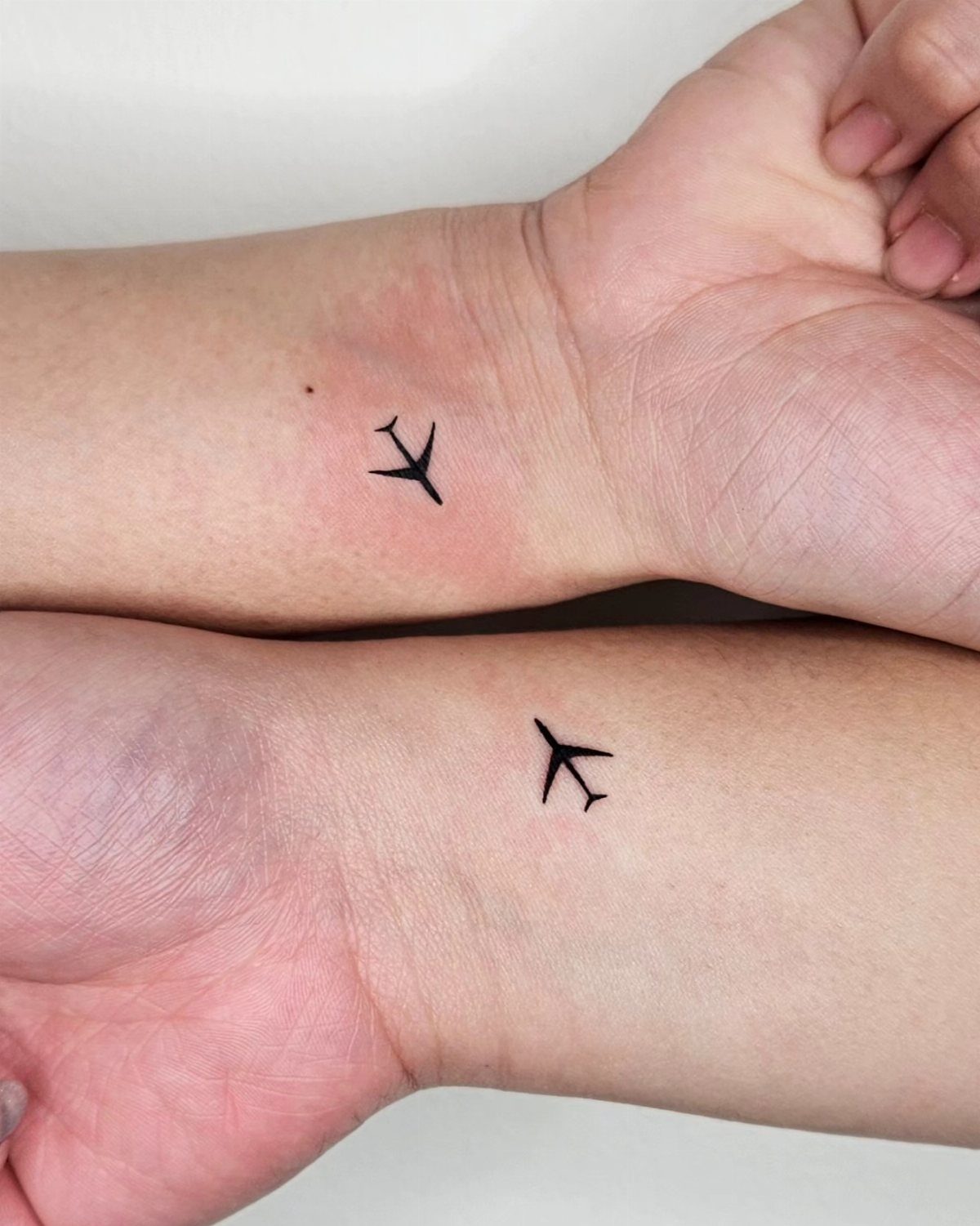 Two inner wrists with small, simple black airplane tattoos.