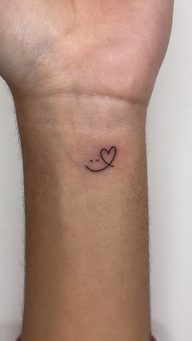 Small black heart tattoo on the inner wrist of a person.
