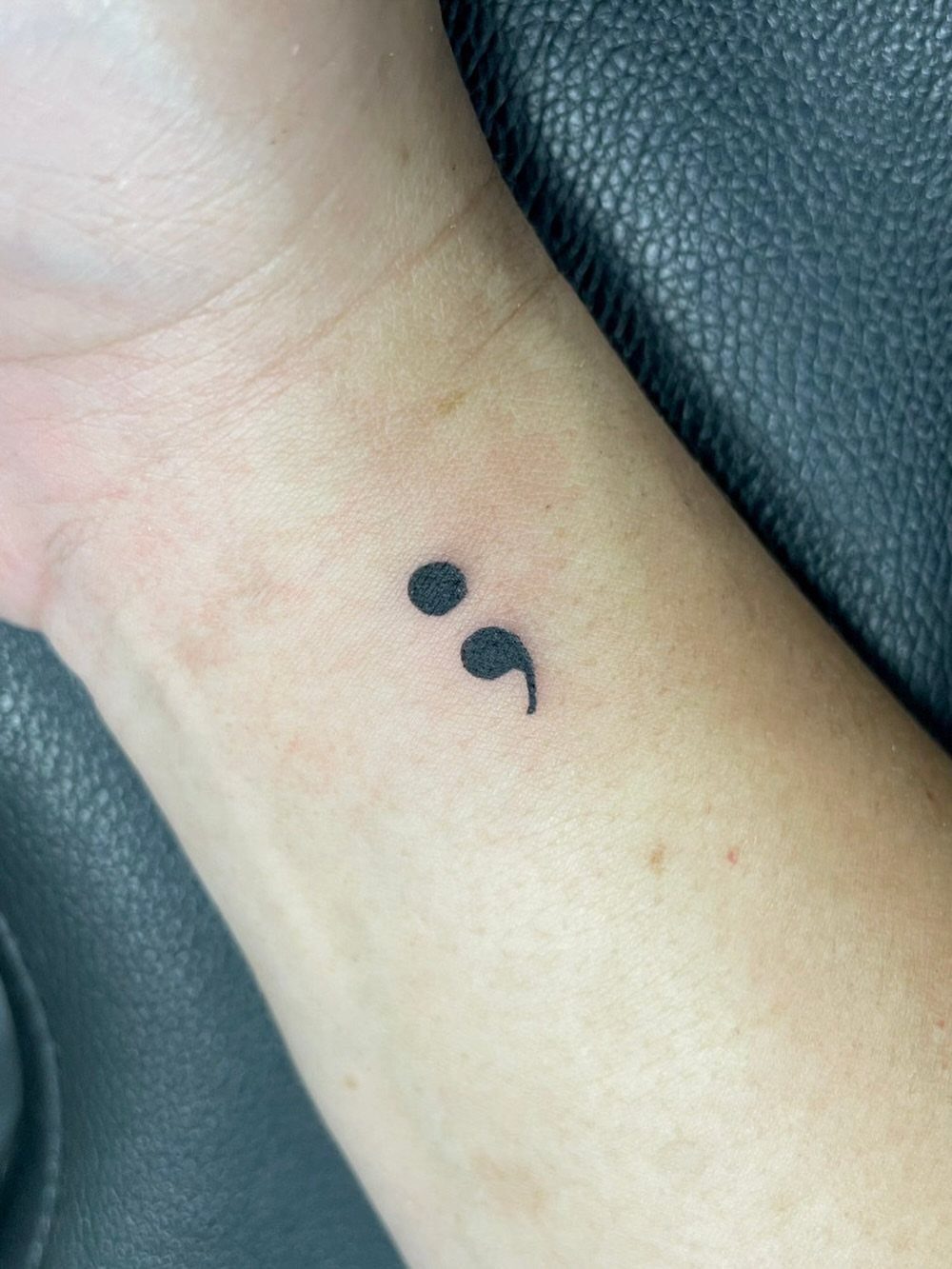 Small black semicolon tattoo on the inner wrist of a person.