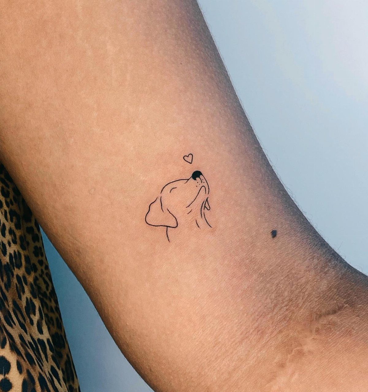 Small minimalist dog head tattoo with a heart on a person's inner wrist.