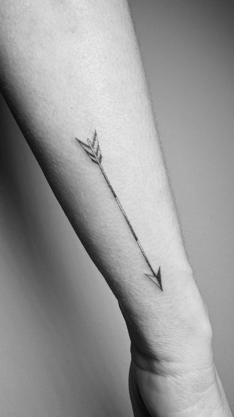 Small black arrow tattoo on the inner wrist and forearm of a person.