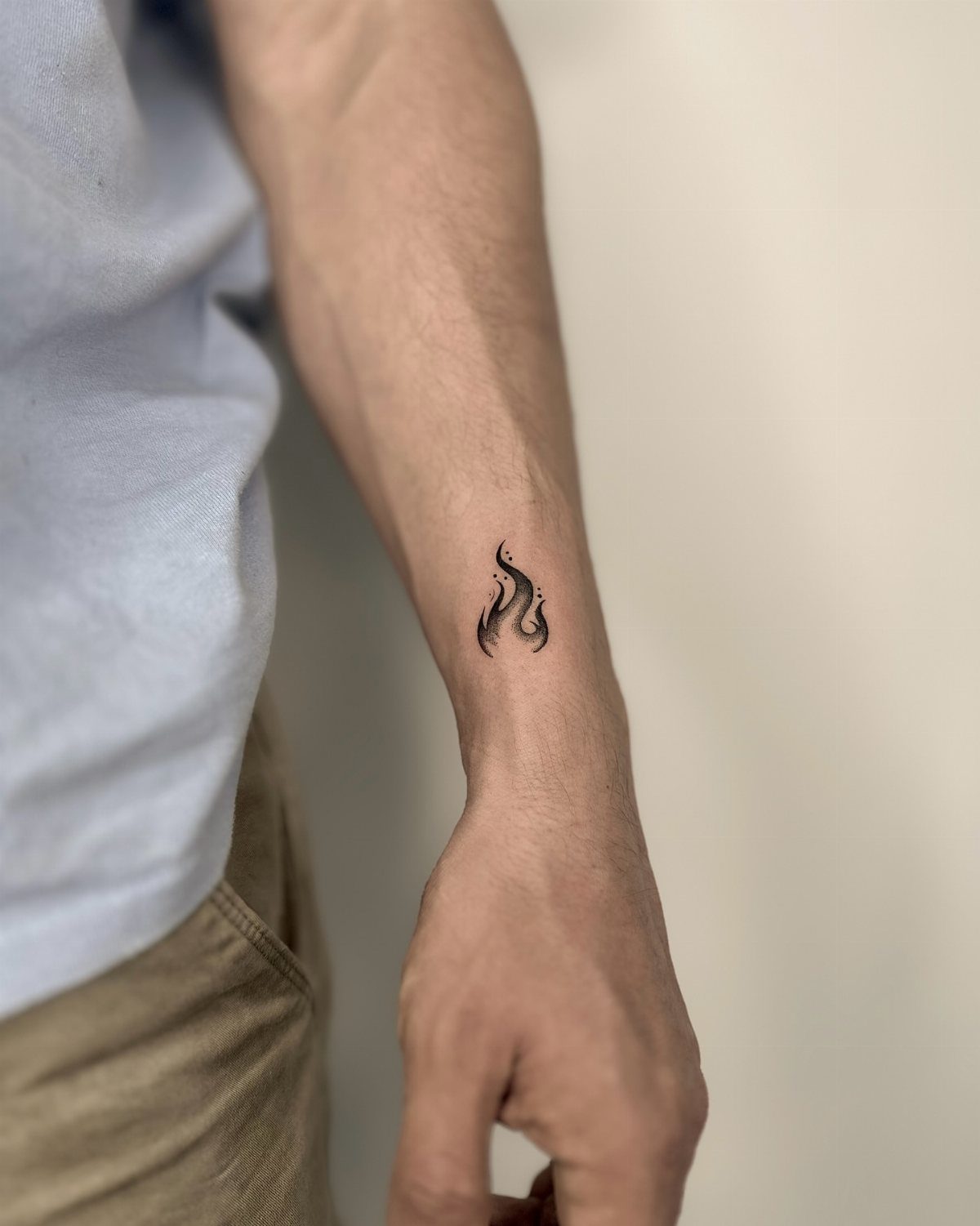 Small black flame tattoo on the inner wrist of a man's arm.