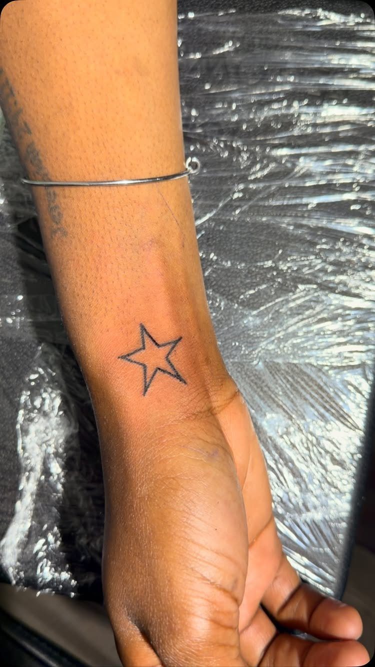 Small black star tattoo on a person's wrist with a thin silver bracelet.