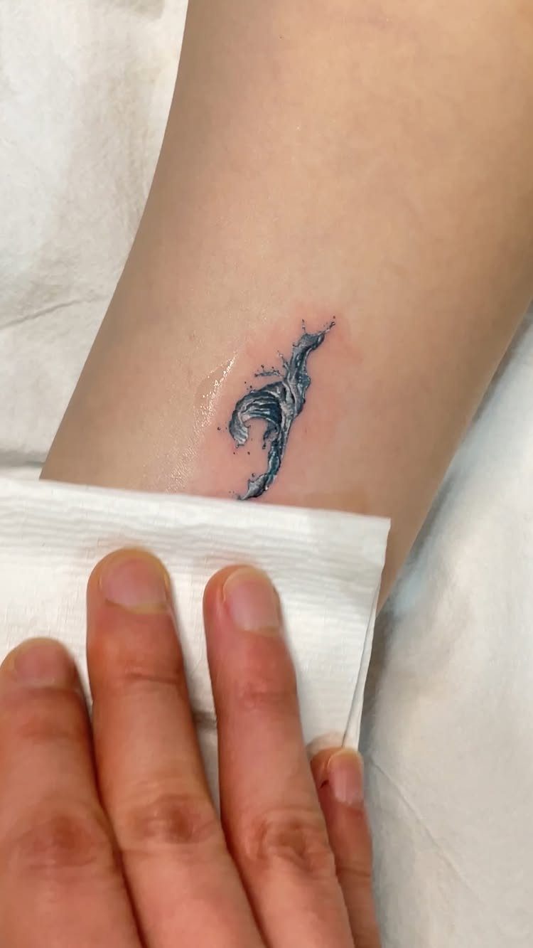 Small blue ocean wave tattoo on the inner wrist of a person.