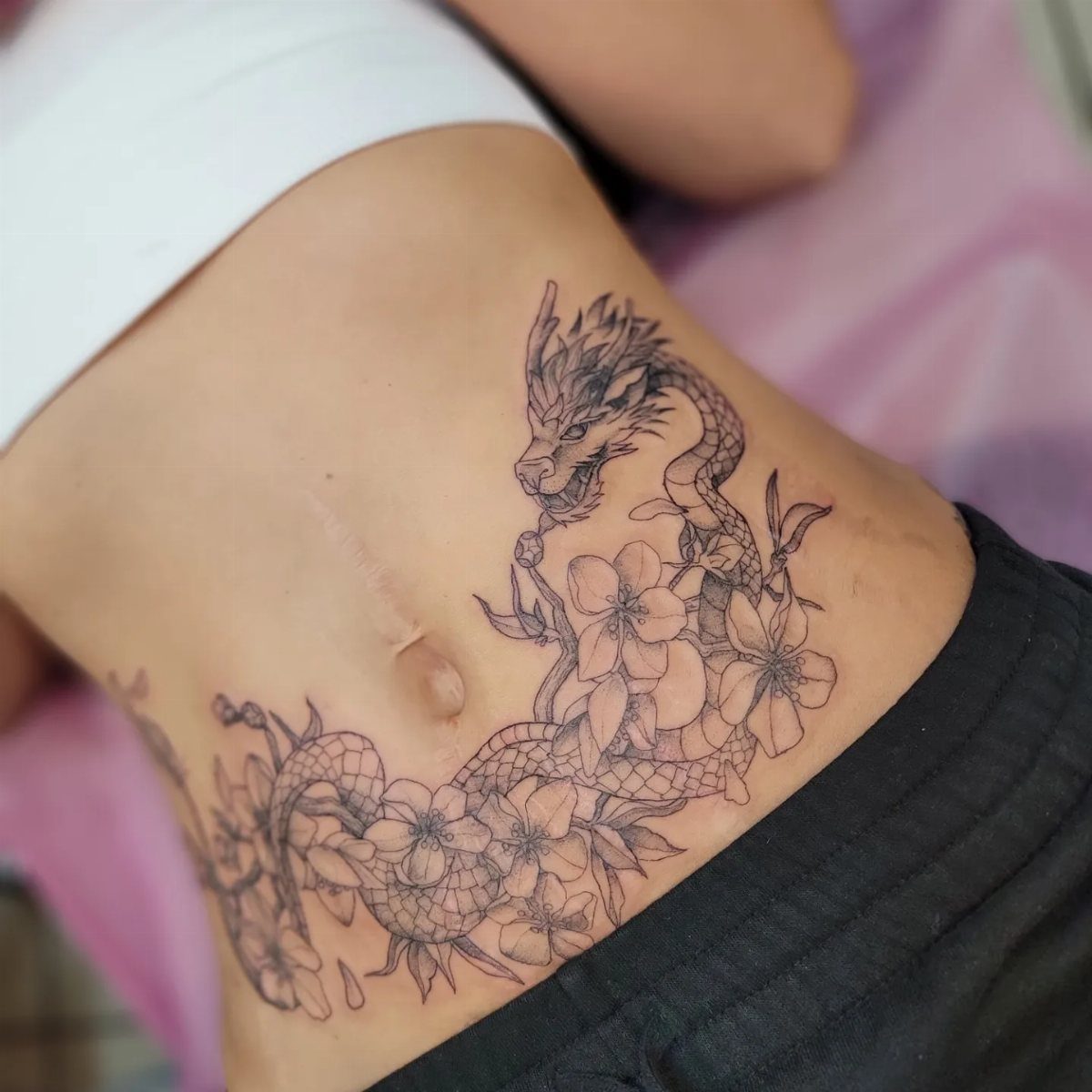 Dragon and cherry blossom tattoo on a woman's stomach in black ink