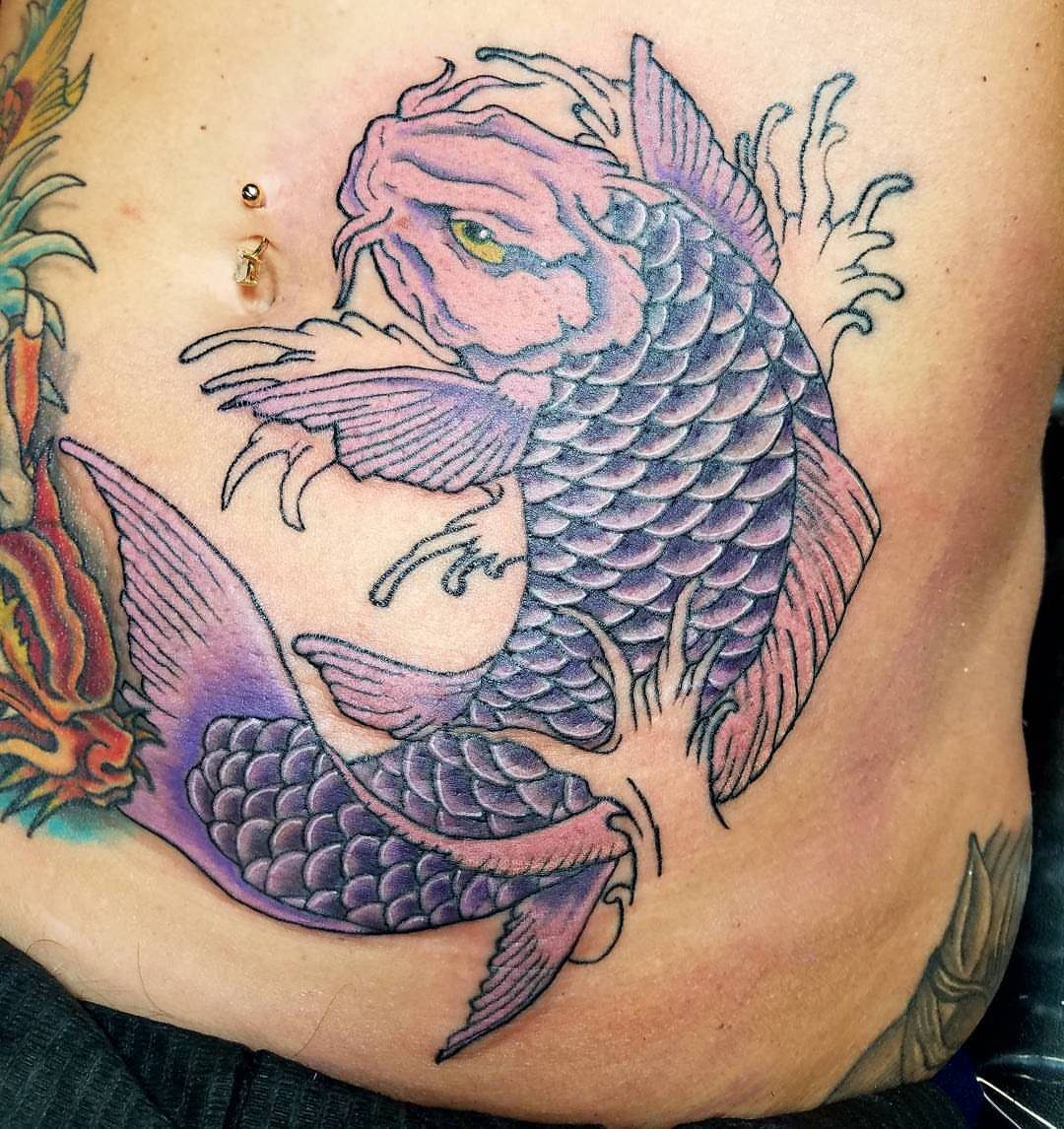 Purple and pink koi fish tattoo on a woman's stomach with water splashes.