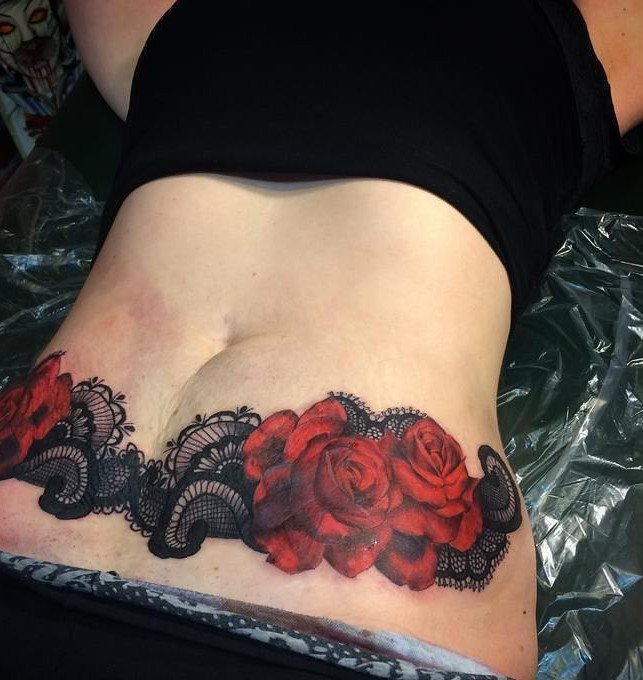 Red rose and black lace tattoo on a woman's lower stomach area