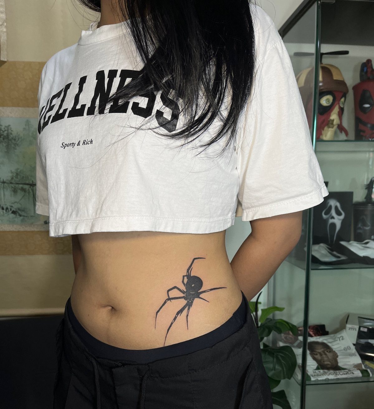 Woman with a realistic black spider tattoo on her lower stomach area.