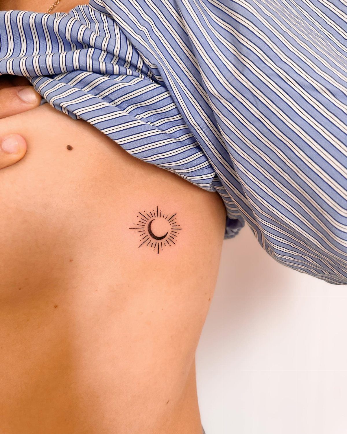 Sun and moon tattoo on a person's stomach with a striped shirt lifted.