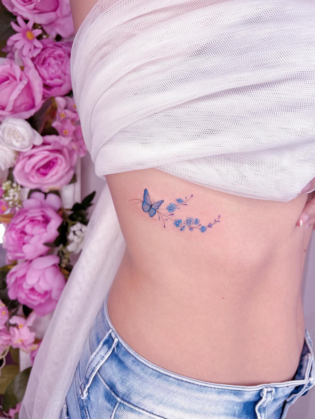 Blue watercolor butterfly tattoo with small flowers on a woman's stomach.