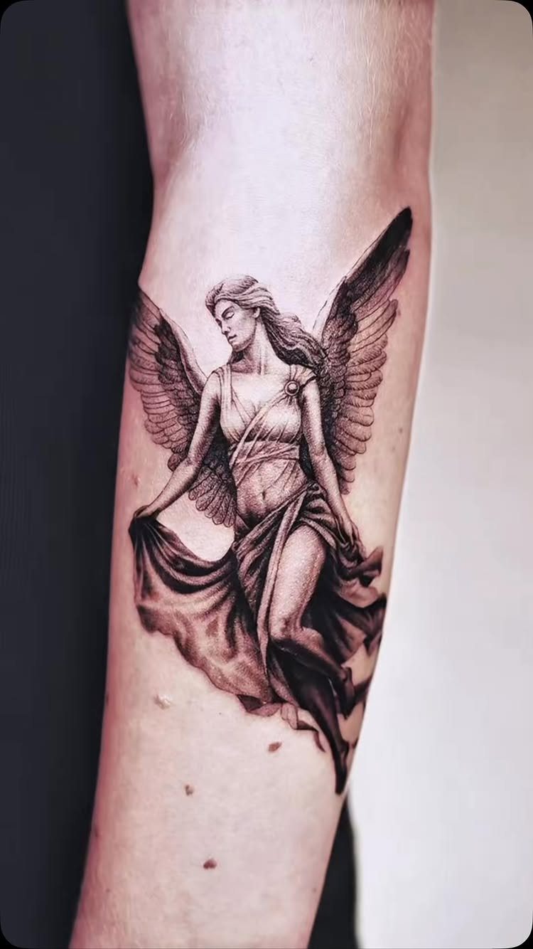 Angel tattoo with large wings and flowing robes on a person's forearm.