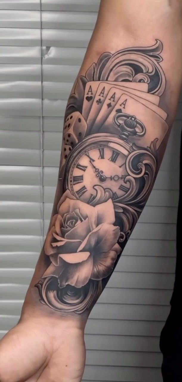 Forearm tattoo featuring a detailed pocket watch, rose, and playing cards in black ink.