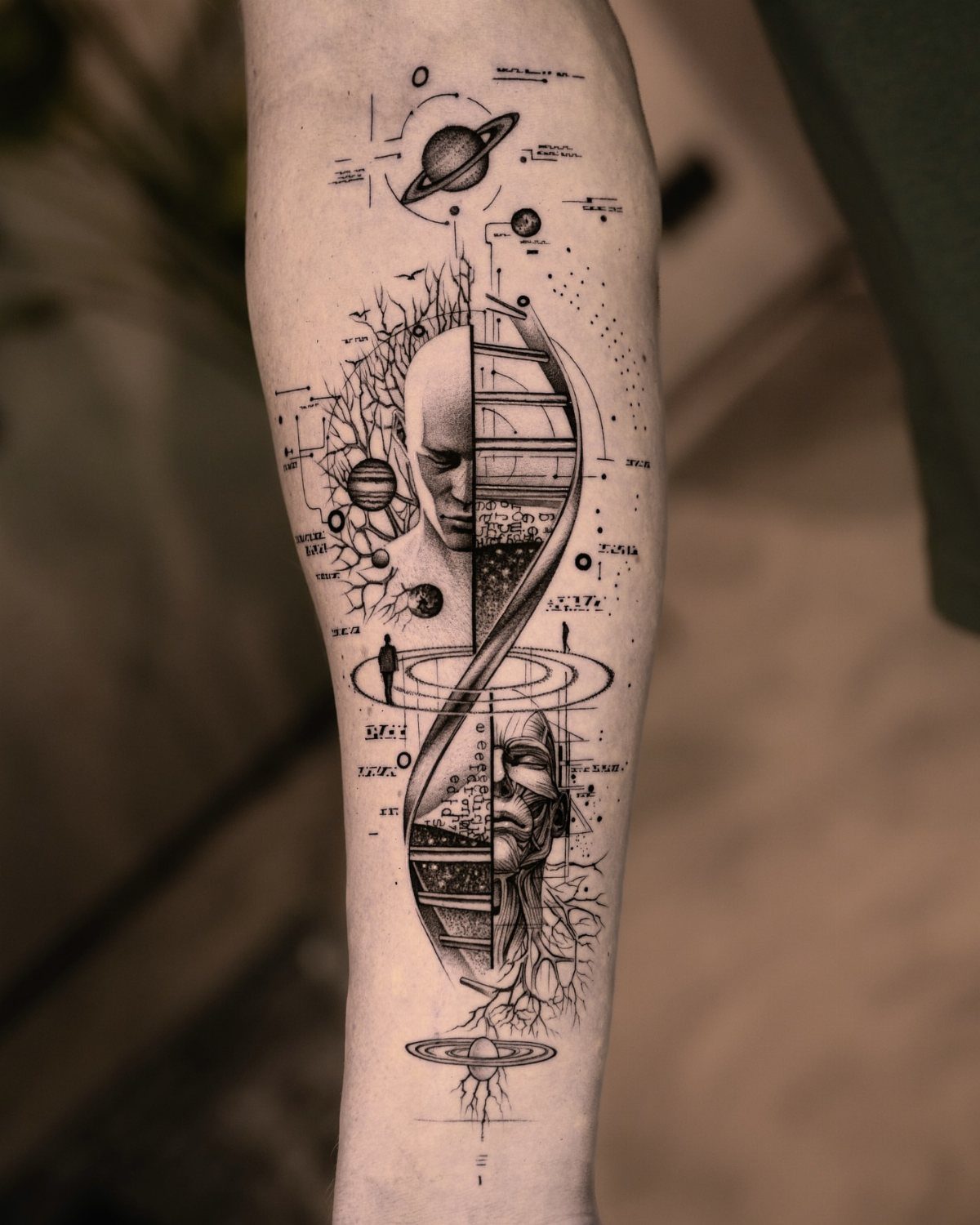 Surreal black ink forearm tattoo featuring planets, a DNA helix, and human faces.