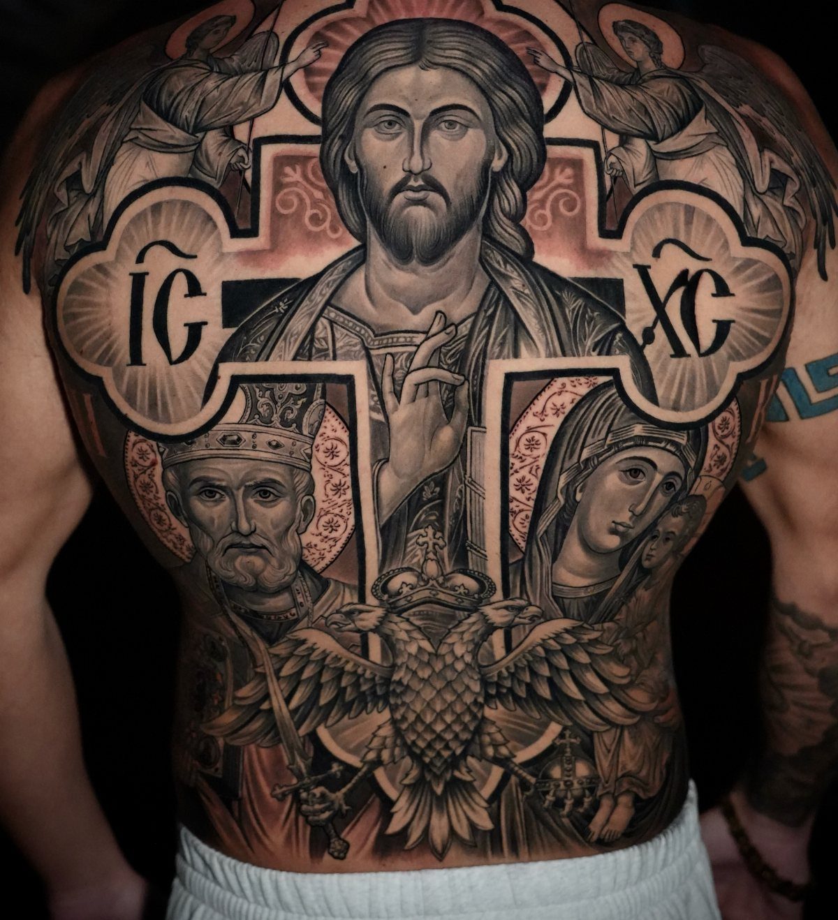 Detailed religious back tattoo featuring Jesus Christ within a large ornate cross frame.