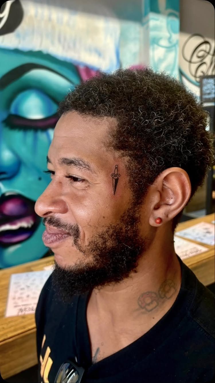 Man with a small black dagger tattoo on his temple and neck tattoos.