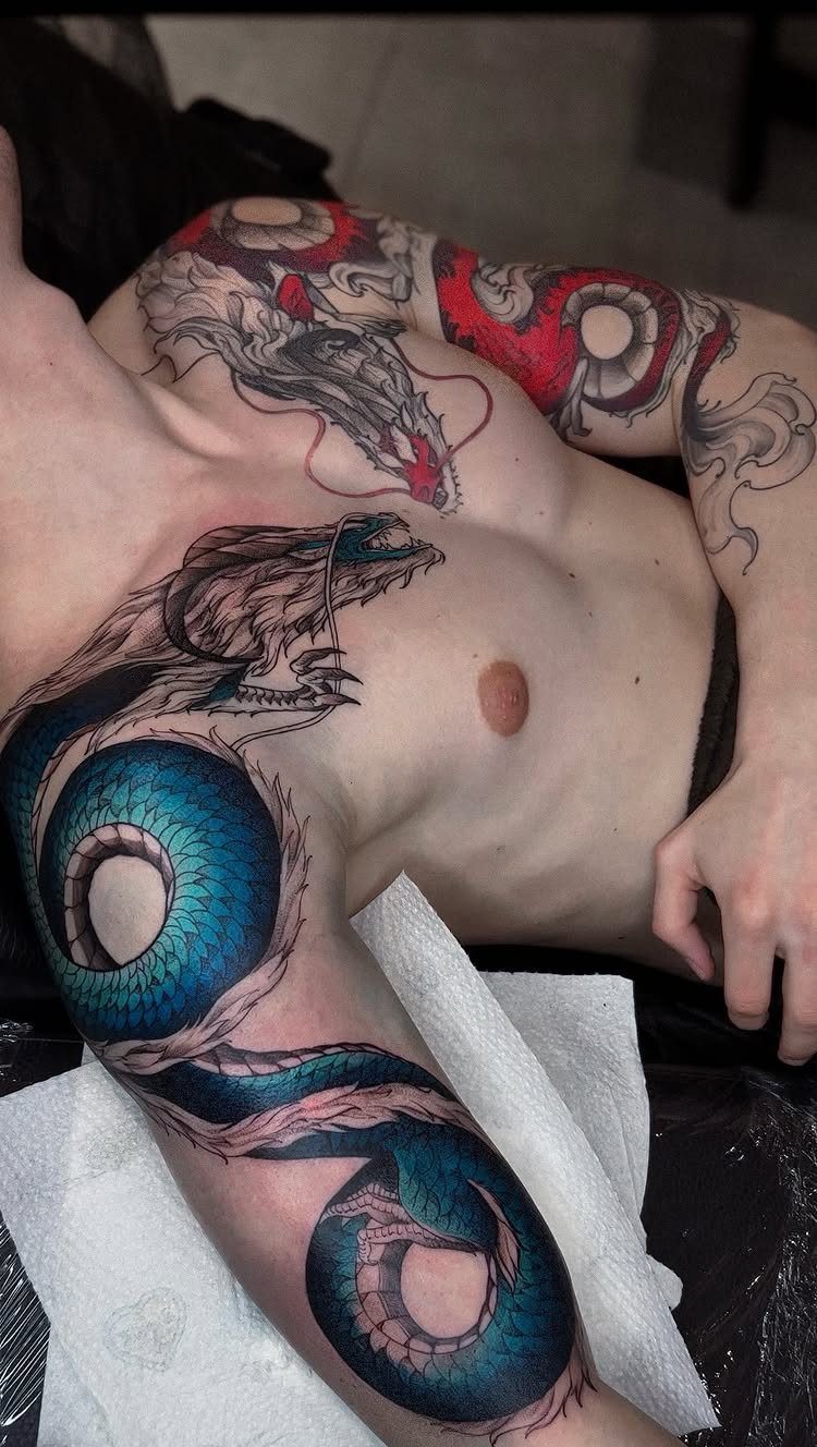 Detailed blue and red dragon tattoos winding across a man's chest and arm.