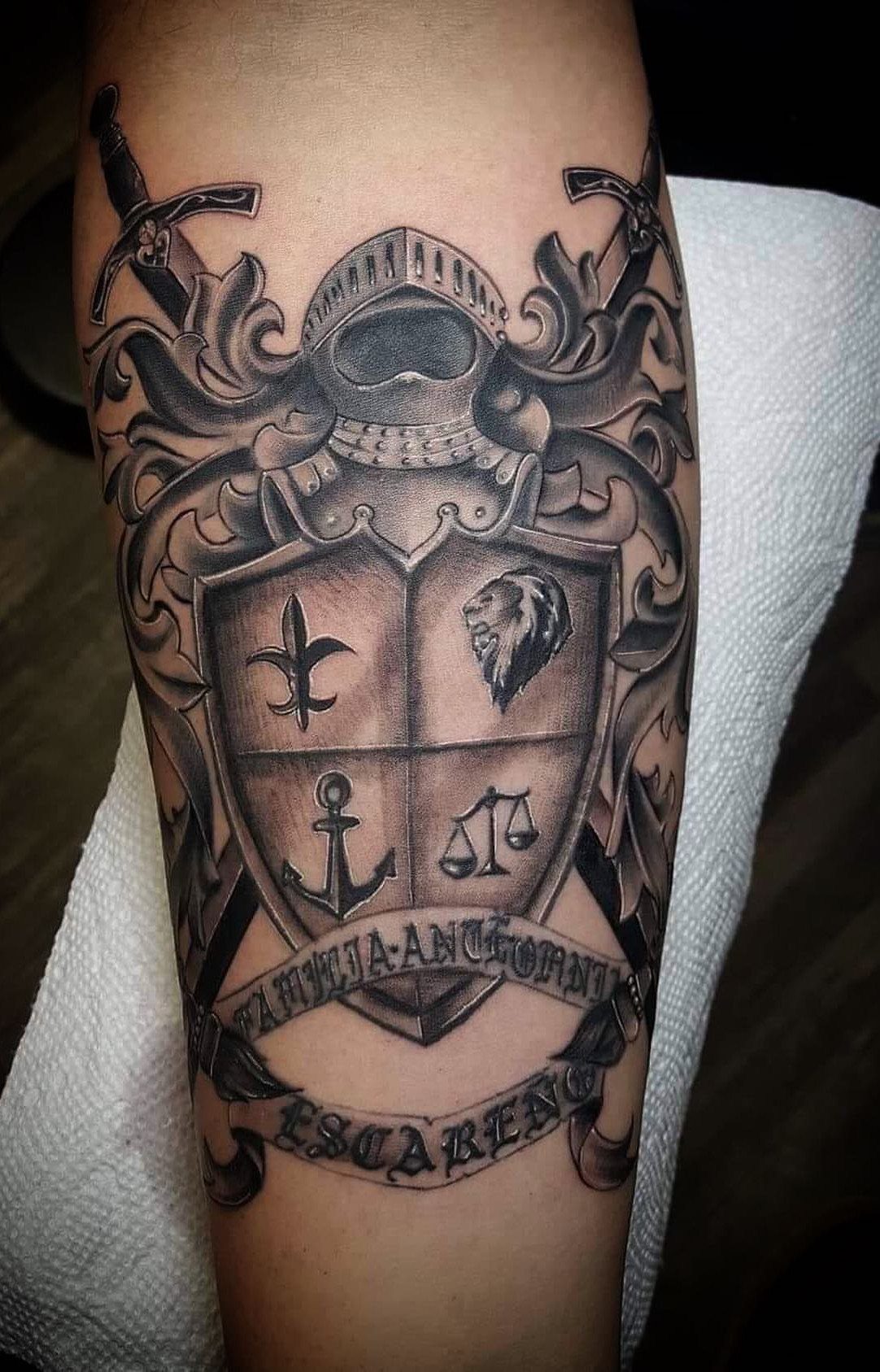 Heraldic shield tattoo with knight helmet and swords on a man's arm.
