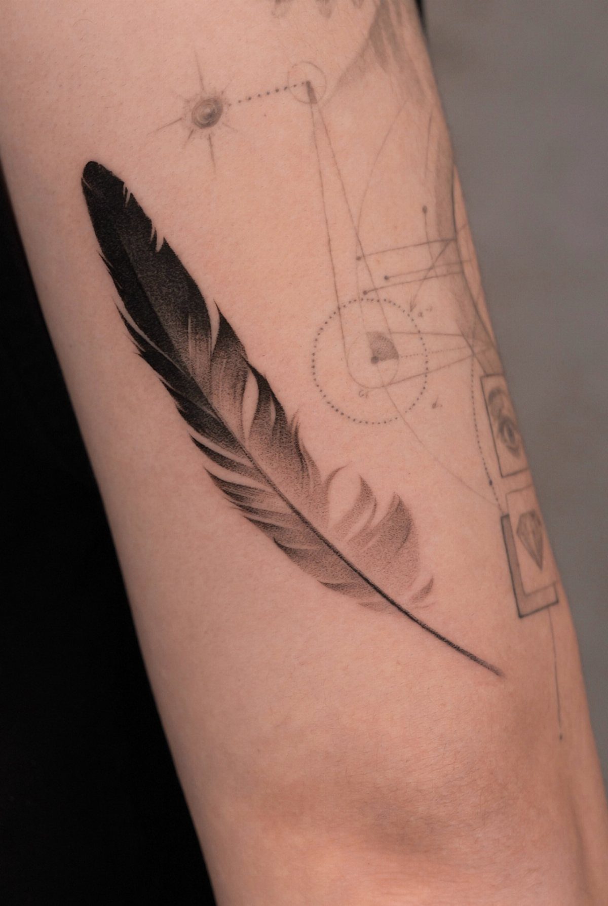 Detailed black ink feather tattoo on a person's arm with geometric line art.